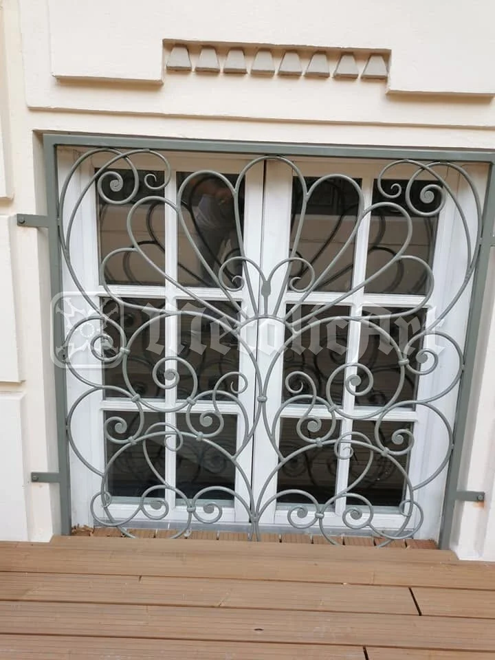 Grilaj cu volute la fereastra de la parter, pe fațada cu brâuri.