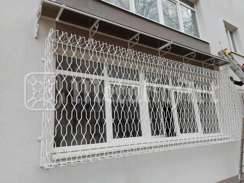 Grilaj alb cu împletitură, la fereastra de la parterul blocului.