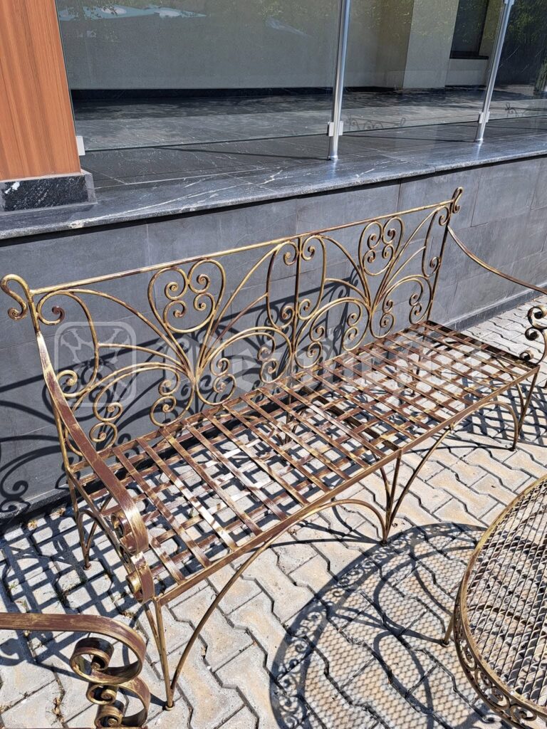 Bancheta aurie cu spătar de volute, pe terasa pavată.