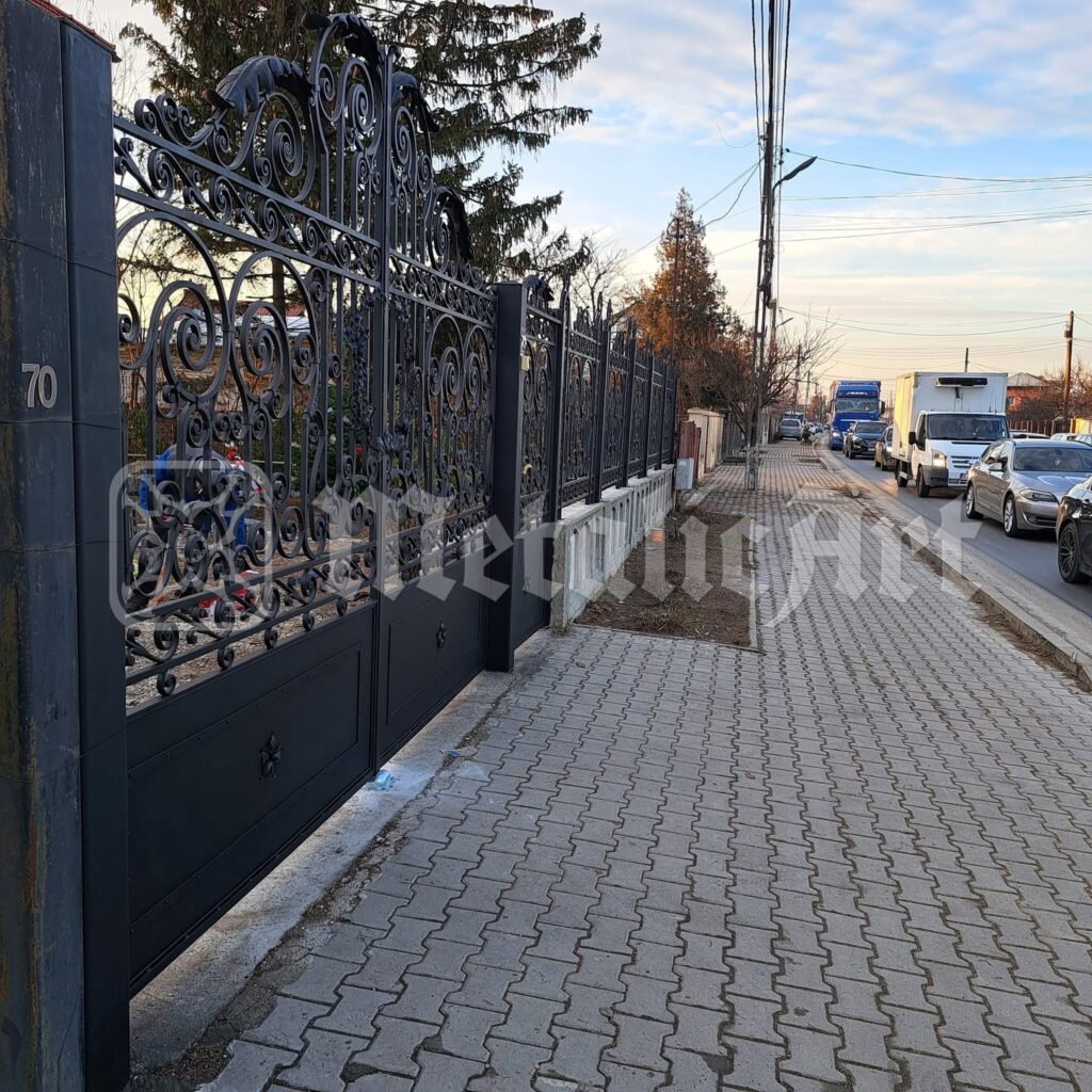 Poarta și gardul de-a lungul trotuarului, în lumina serii.