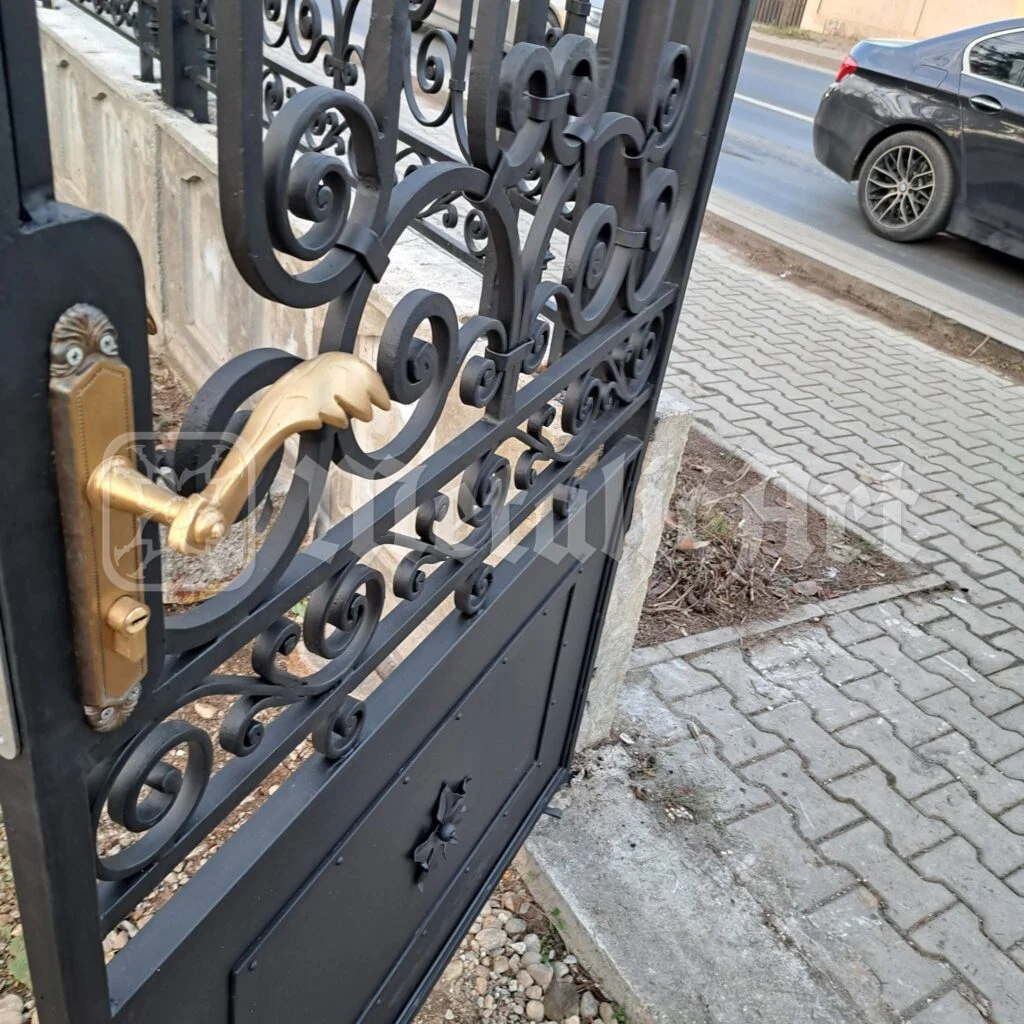 Mânerul de alamă al portiței, cu volutele din jurul lui.