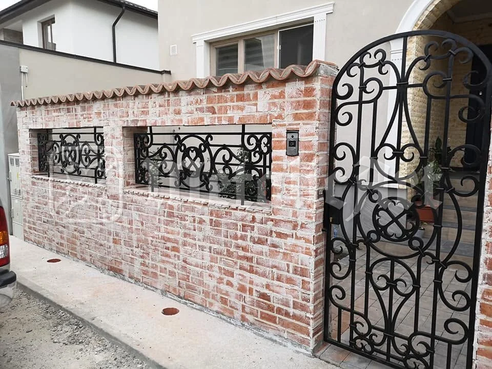 Portița arcuită din zidul de cărămidă, deschisă spre alee.