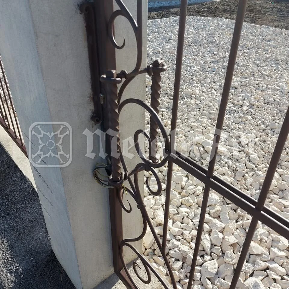 Portița în grund, prinsă în balamale, cu pietrișul curții dedesubt.