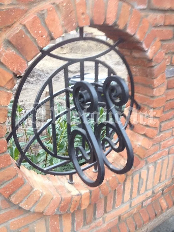 Medalion rotund de fier forjat, în golul zidului de cărămidă.