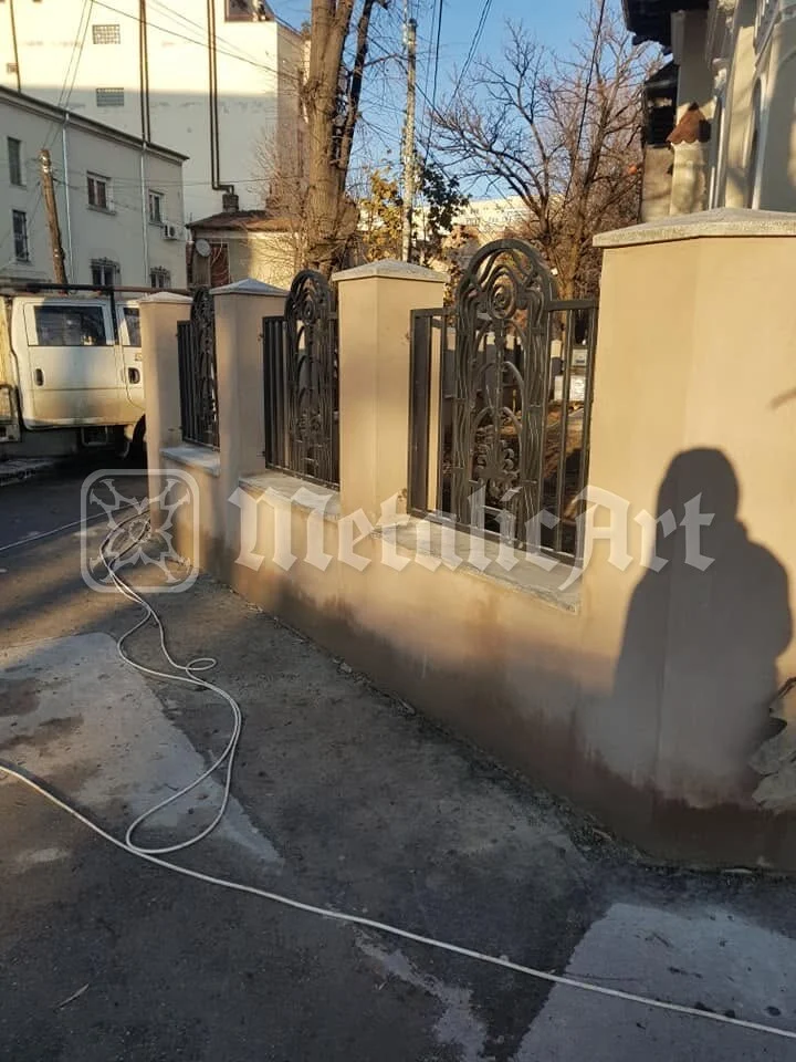 Gardul de-a lungul trotuarului, cu stâlpii de beton.
