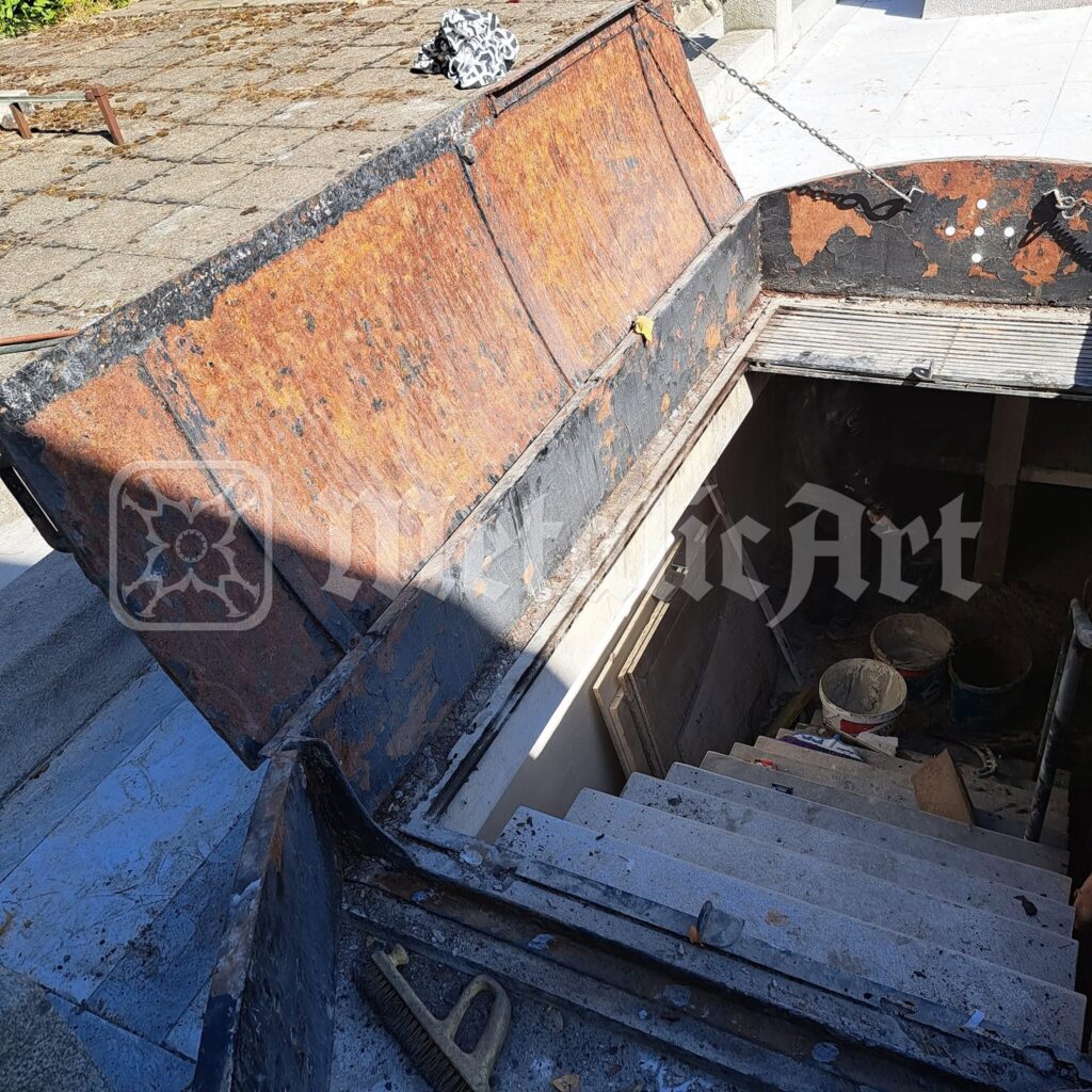 Capacul vechi, ruginit, ridicat deasupra scării criptei, înainte de restaurare.