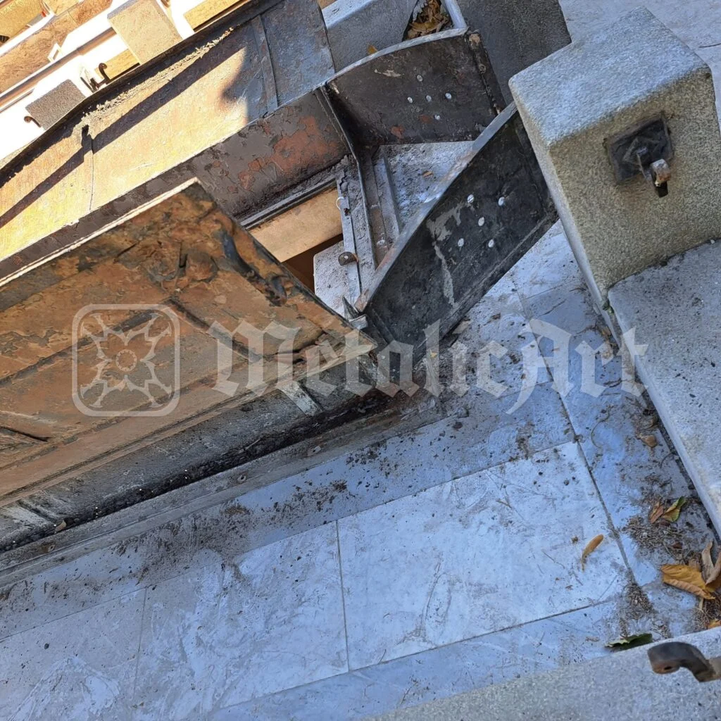 Cripta deschisă, cu lespezile de marmură și canatul de tablă ridicat lângă stâlpul de granit.