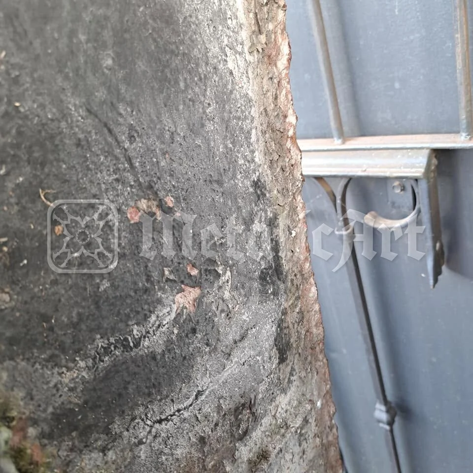 Zidăria cavoului, cu tencuiala căzută, lângă canatul de tablă și zăvorul lui.