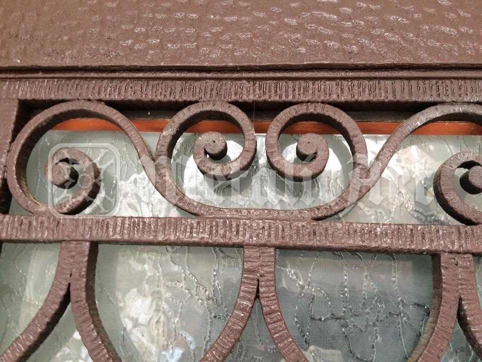 Brâul de volute de sub arc, cu barele martelate, peste geamul cu model.